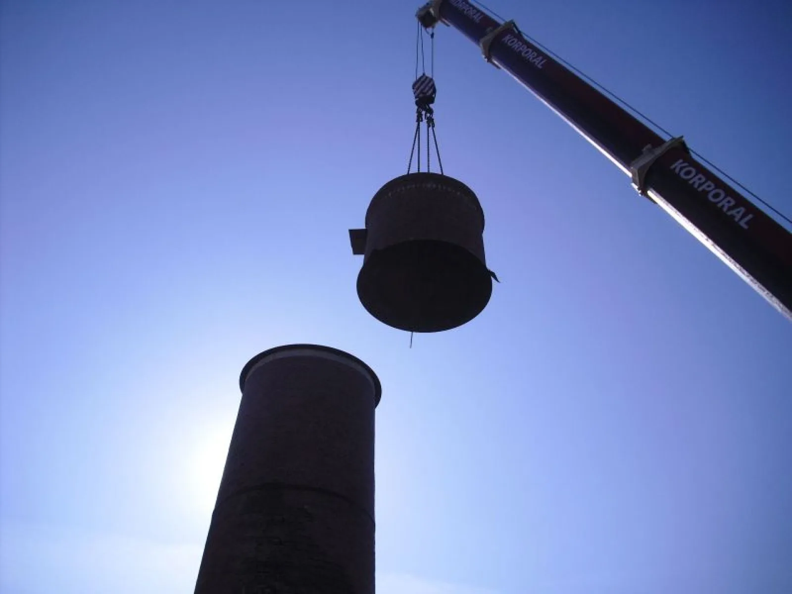 Korporal Autokran hebt ein Schornsteinsegment vor blauem Himmel